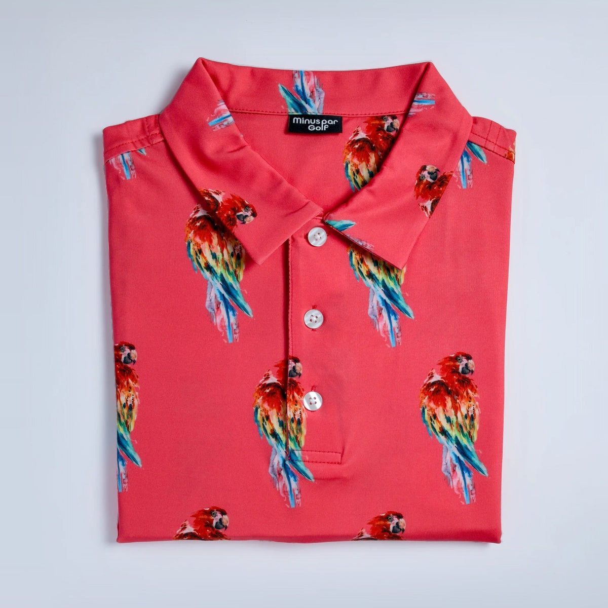 Parrot golf polo in coral with a rainbow parrot print, folded